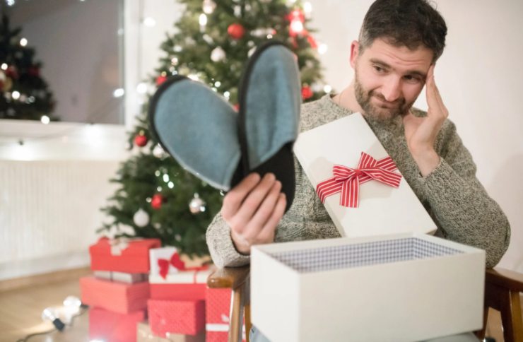 uomo deluso che trova delle pantofole dentro ad un pacco di natale
