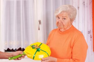 donna anziana con espressione delusa mentre le consegnano una padella in regalo